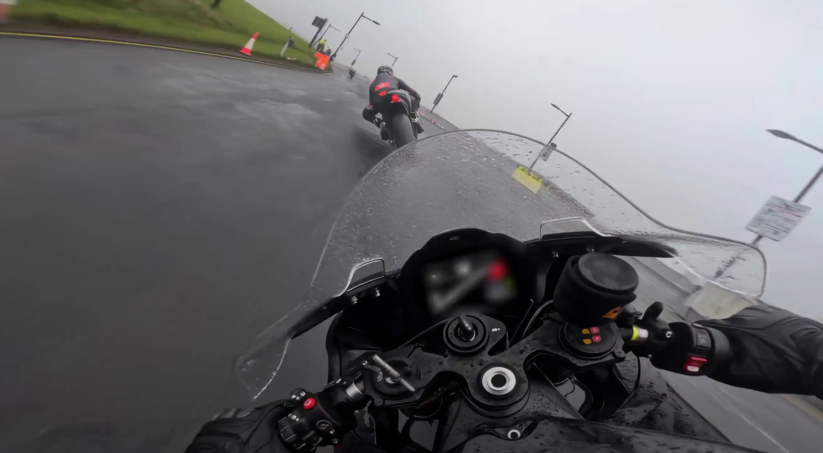 First-person motorcycle view following another rider around a rain-soaked track