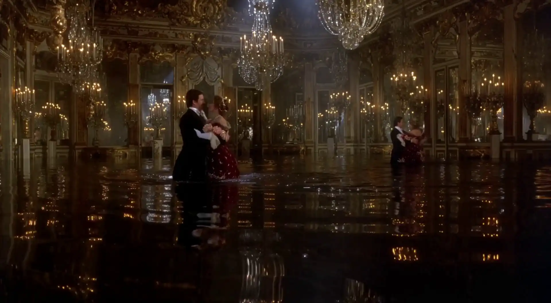 A formally dressed couple dancing in an ornate mirrored ballroom illuminated by chandeliers