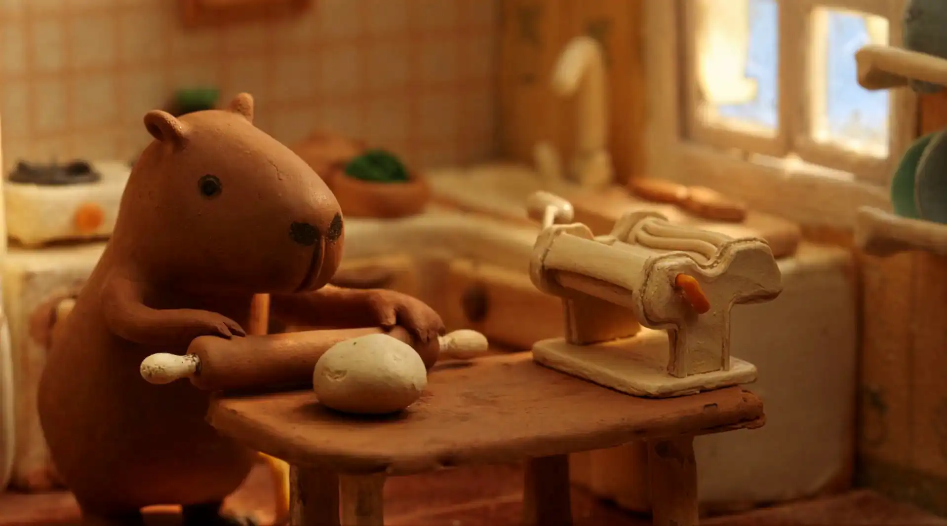 A clay bear character preparing dough beside a miniature pasta machine in a warm kitchen